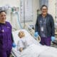 Two licensed practical nursing students pose next to practice mannequin in hospital bed